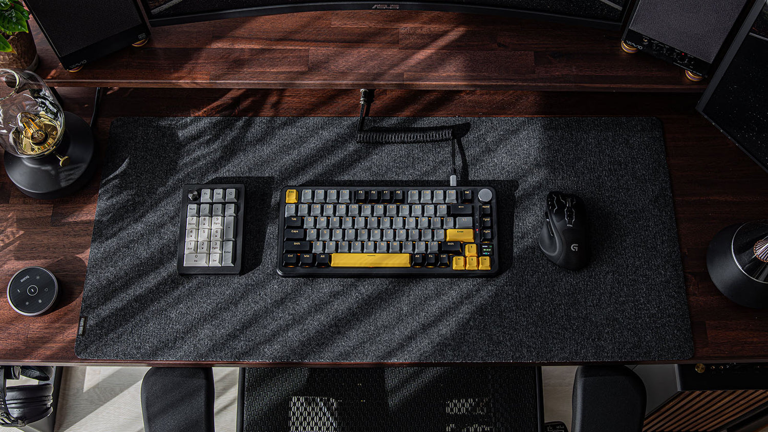 A professional desk setup featuring a 65% mechanical keyboard with black base and yellow accent keycaps, accompanied by a separate white/silver numpad on the left